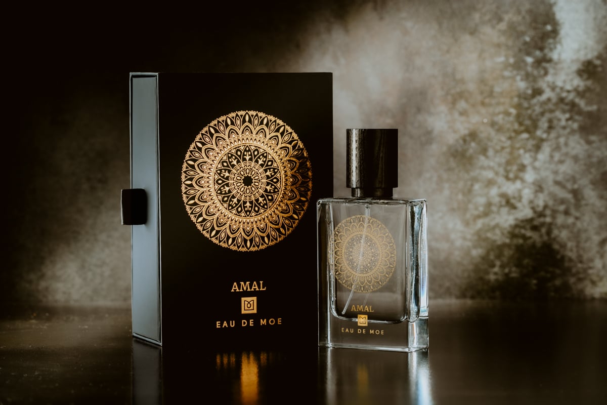 Perfume bottle and packaging with 'AMAL' branding on a dark background