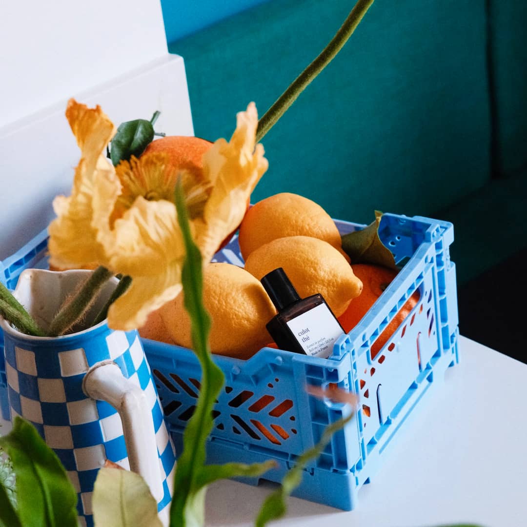 Versatile Paris Culot Thé perfume bottle placed in blue crate with lemons and flowers in bright setting