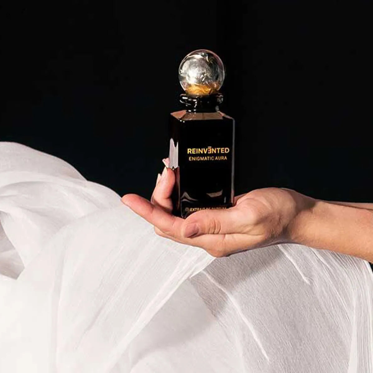 Reinvented Enigmatic Aura extrait de parfum luxury niche fragrance bottle with marble cap held in hand lifestyle close-up