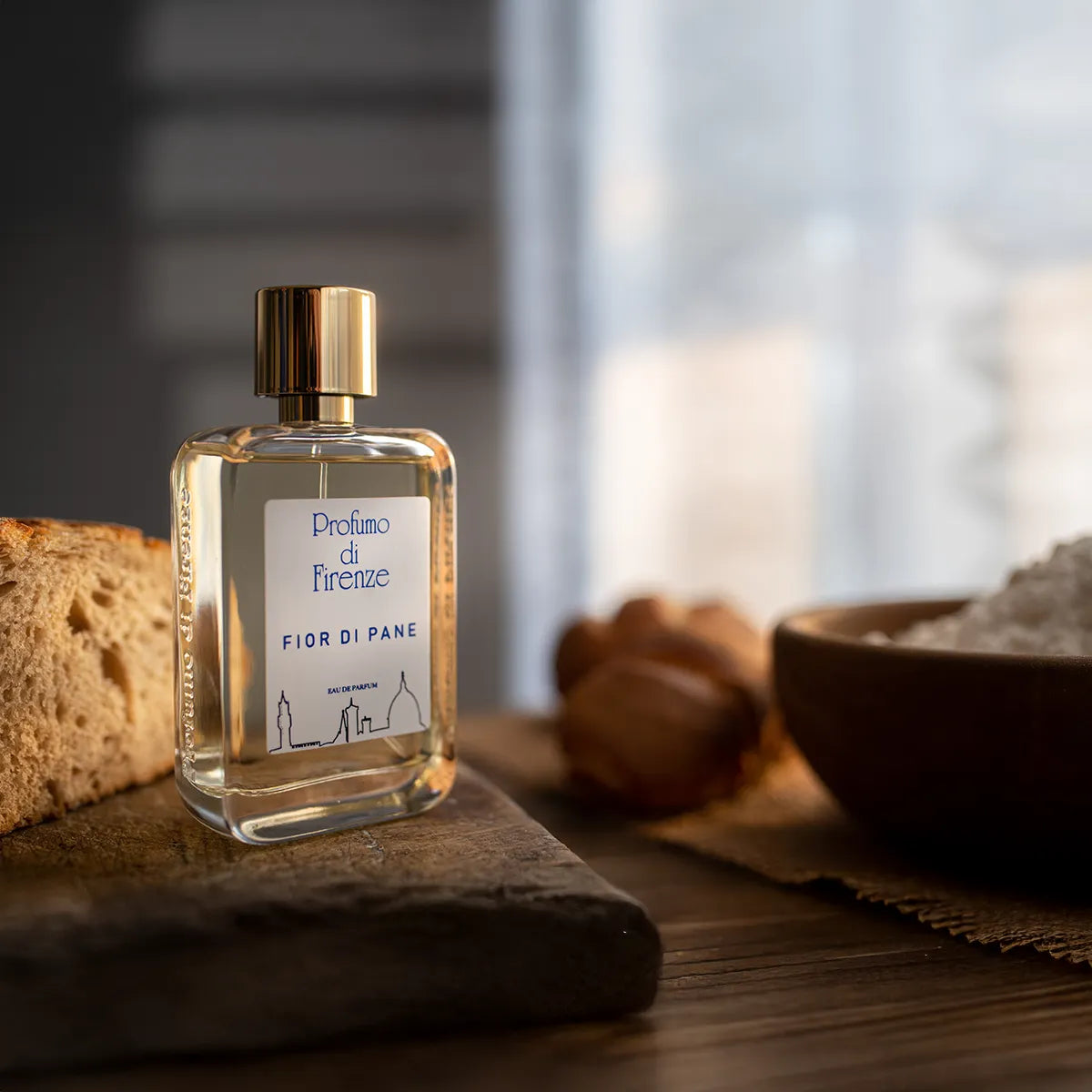 Perfume bottle labeled 'Profumo di Firenze' on a wooden surface with bread and a bowl in the background.