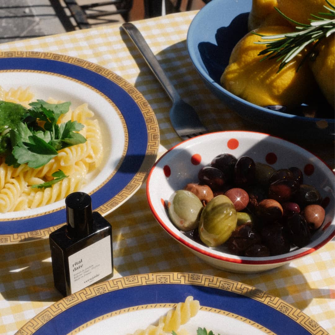 Versatile Paris Rital Date perfume bottle on dining table with pasta, olives, and lemons in sunny setting