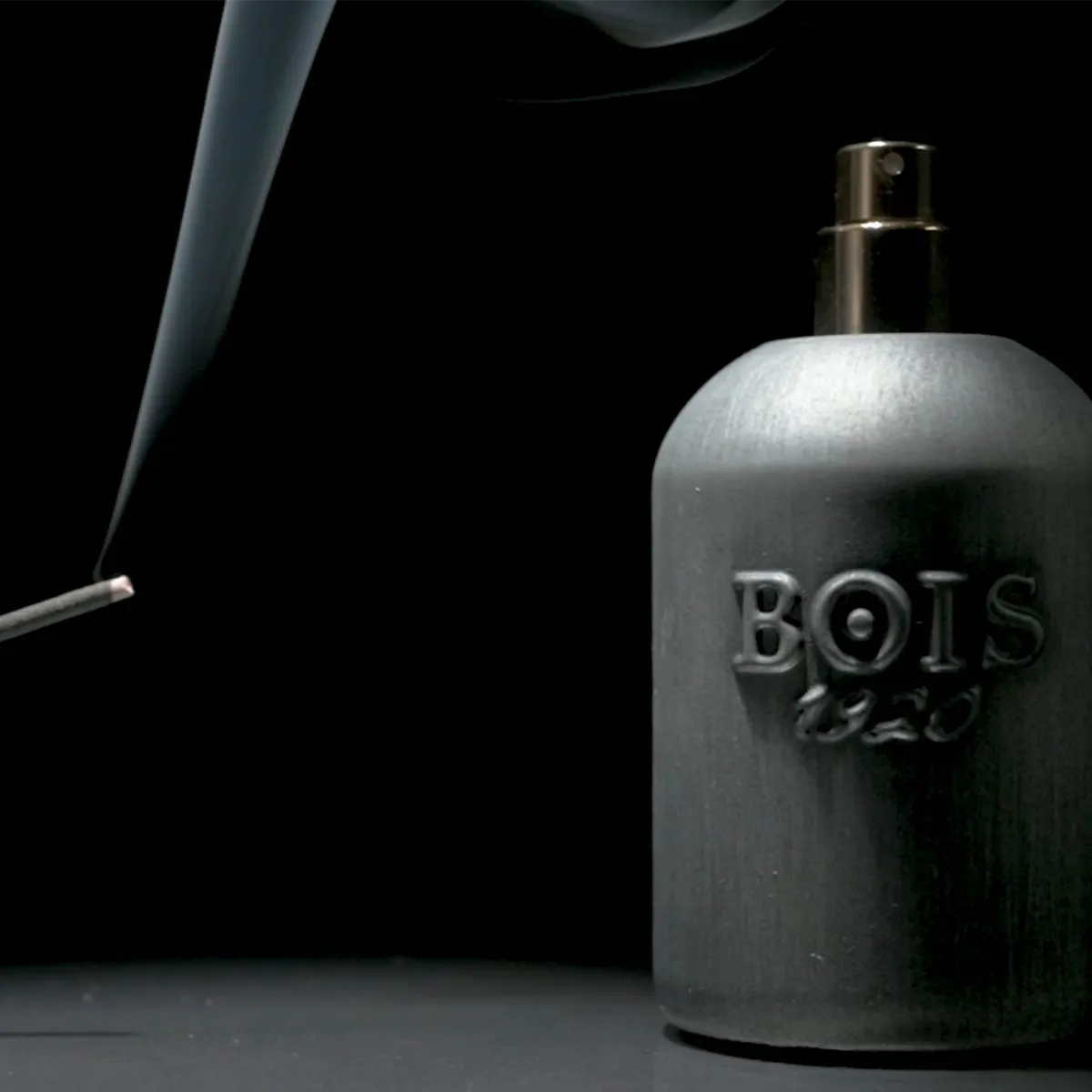 Bois 1920 Scuro perfume bottle with dark brushed metal finish and atomizer beside rising incense smoke on a black background.