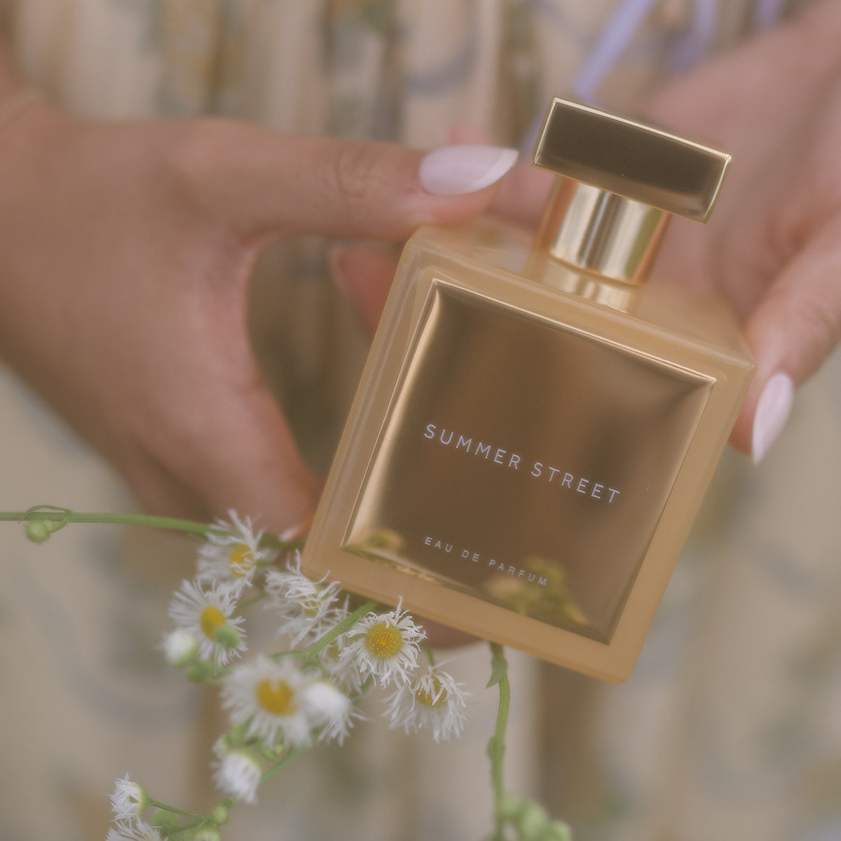 Elegant shot of Summer Street perfume held by hand with white flowers, golden amber fragrance | Hallburg