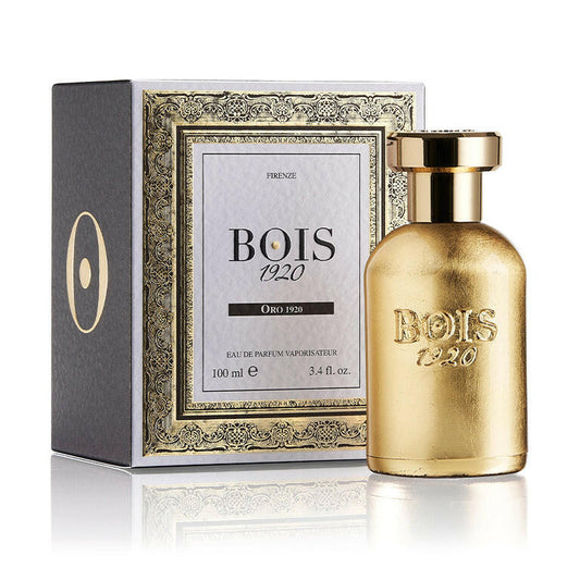 A gold-colored perfume bottle with a white label that reads 'BOIS 1920' and 'ORO'. The bottle is in front of a box with a similar design and the year '1920' visible on it.