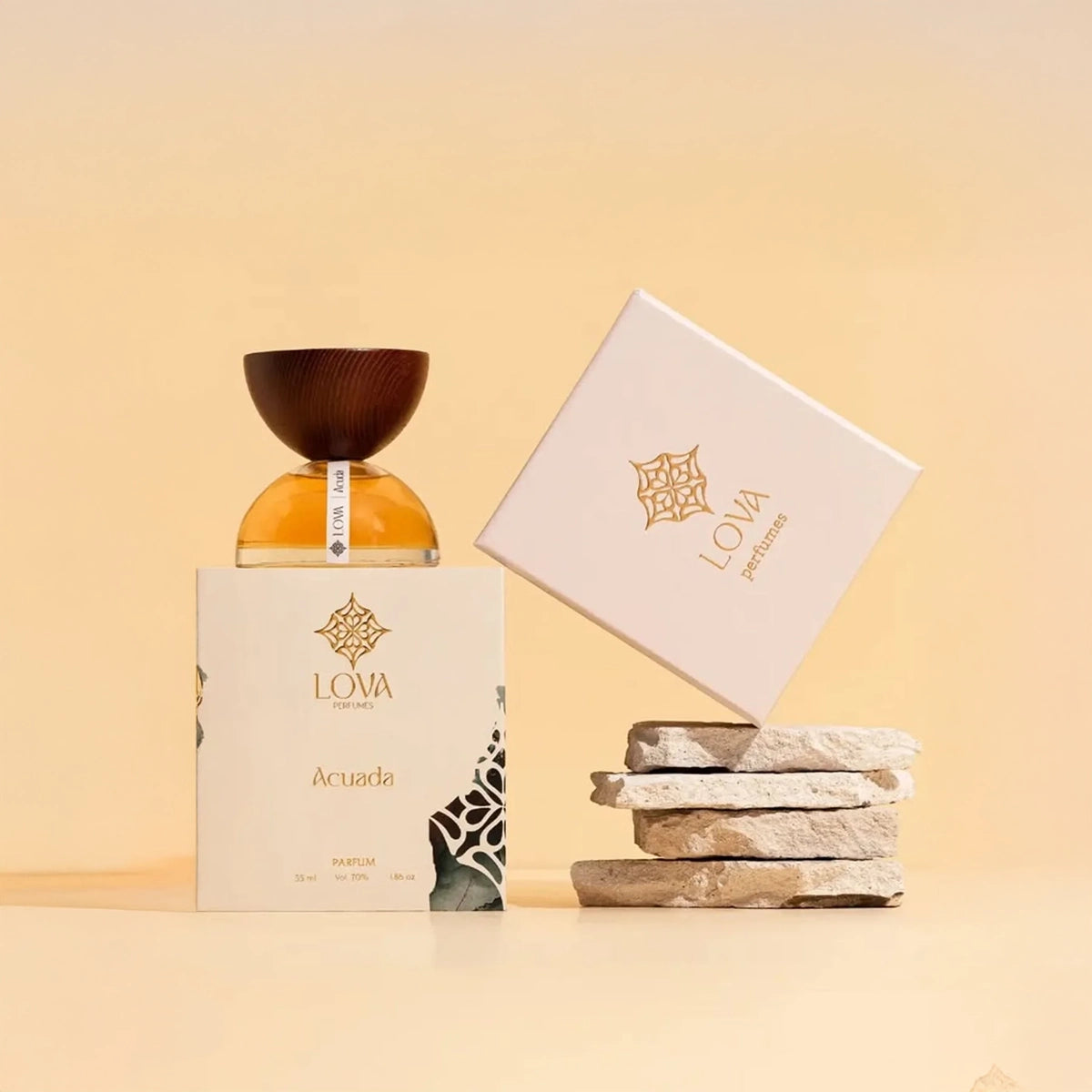 Acuada by LOVA parfum bottle displayed with branded box and stacked stone props against warm beige background