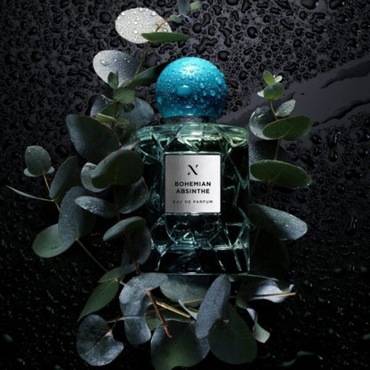 Bohemian Absinthe Eau de Parfum by Les Sœurs de Noé luxury fragrance bottle with turquoise cap surrounded by fresh green leaves and water droplets on dark background