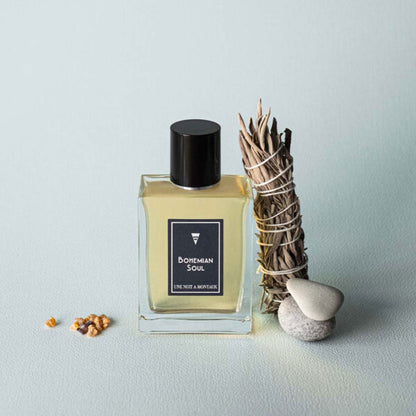 Une Nuit Nomade Bohemian Soul niche perfume bottle beside sage bundle and stones, artistic fragrance composition evoking spiritual, woody, and aromatic bohemian scent inspiration
