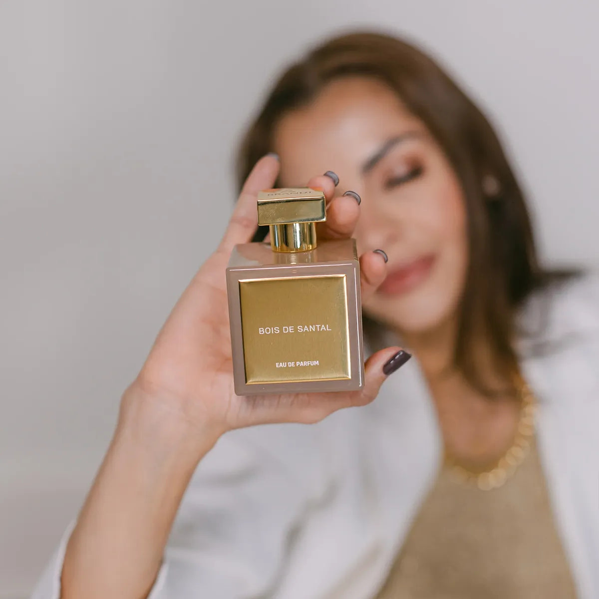 Woman holding Bois de Santal Eau de Parfum by House of Brandt, luxury sandalwood fragrance bottle with gold cap, elegant woody unisex perfume lifestyle image