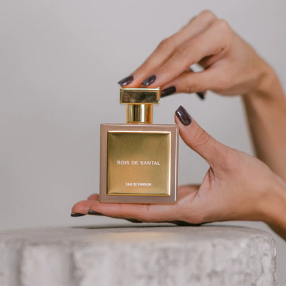 Hands holding and opening Bois de Santal Eau de Parfum by House of Brandt, luxury sandalwood perfume bottle with gold cap, elegant woody unisex fragrance close-up