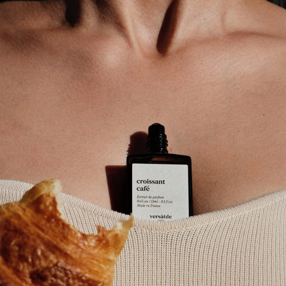 Versatile Paris Croissant Café perfume bottle placed on skin with bitten croissant in foreground