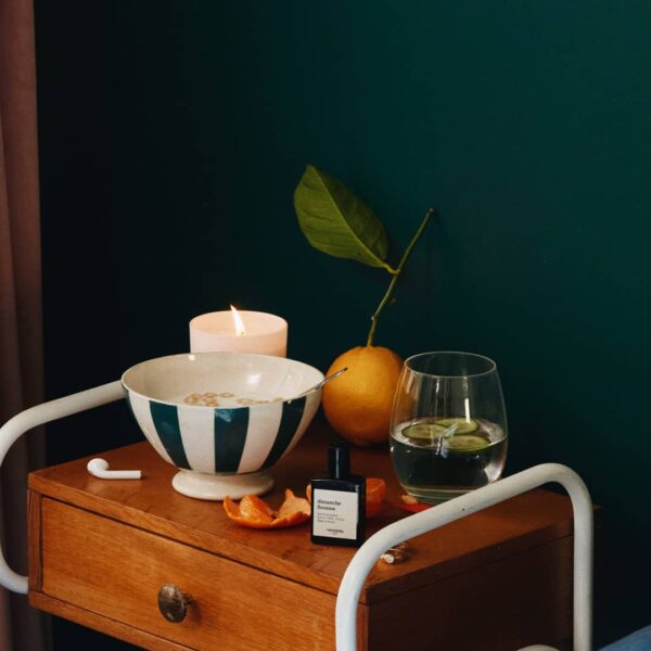 Versatile Paris Dimanche Flemme perfume bottle on wooden table with candle, citrus fruit, and glass of water in cozy setting