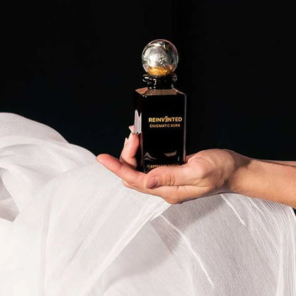 Reinvented Enigmatic Aura extrait de parfum luxury niche fragrance bottle with marble cap held in hand lifestyle close-up