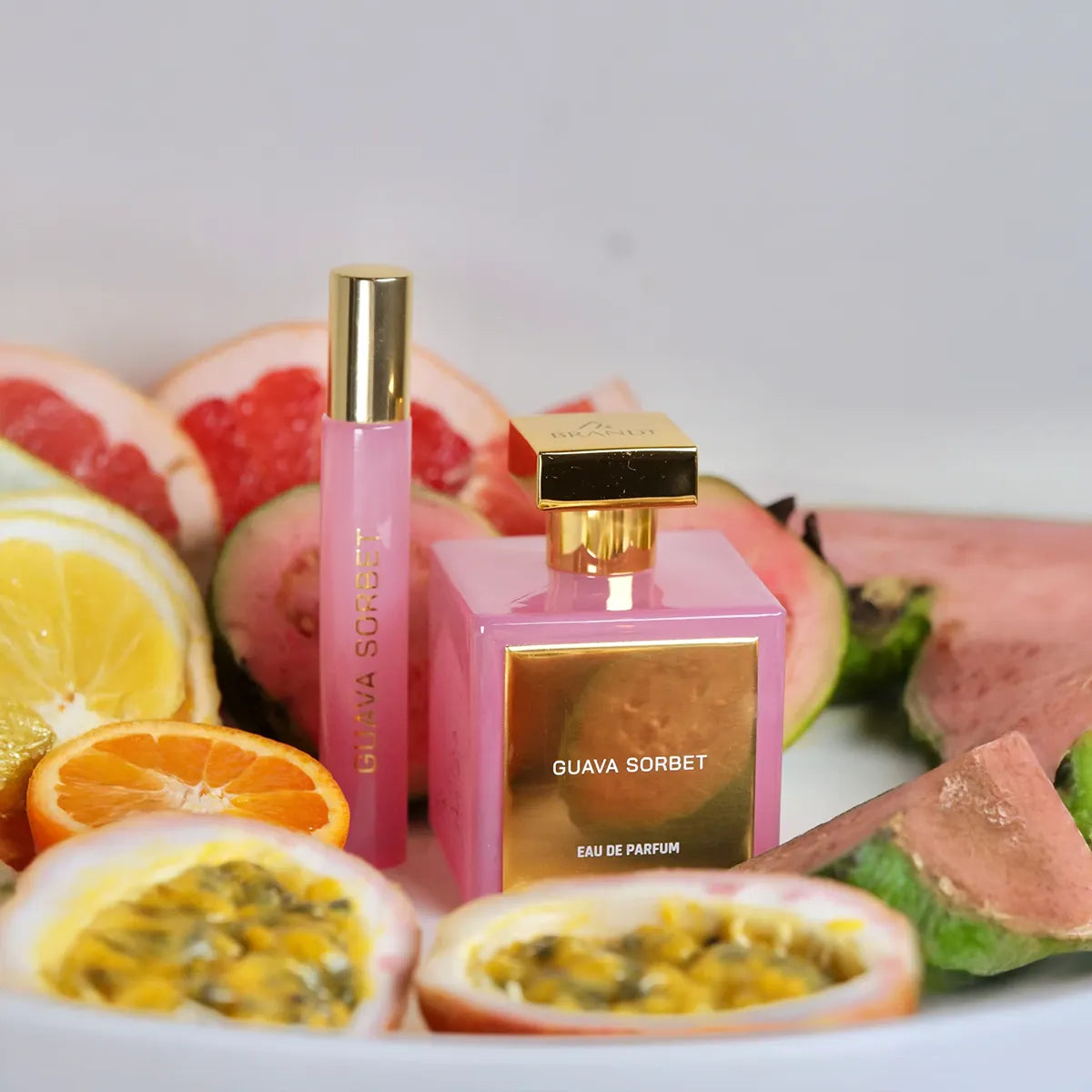 Guava Sorbet Eau de Parfum by House of Brandt pink perfume bottle and travel spray surrounded by fresh guava, citrus and tropical fruits, luxury summer fragrance lifestyle image