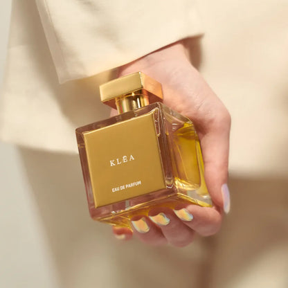 Hand holding KLEA Eau de Parfum by House of Brandt luxury glass perfume bottle with gold cap and amber fragrance liquid