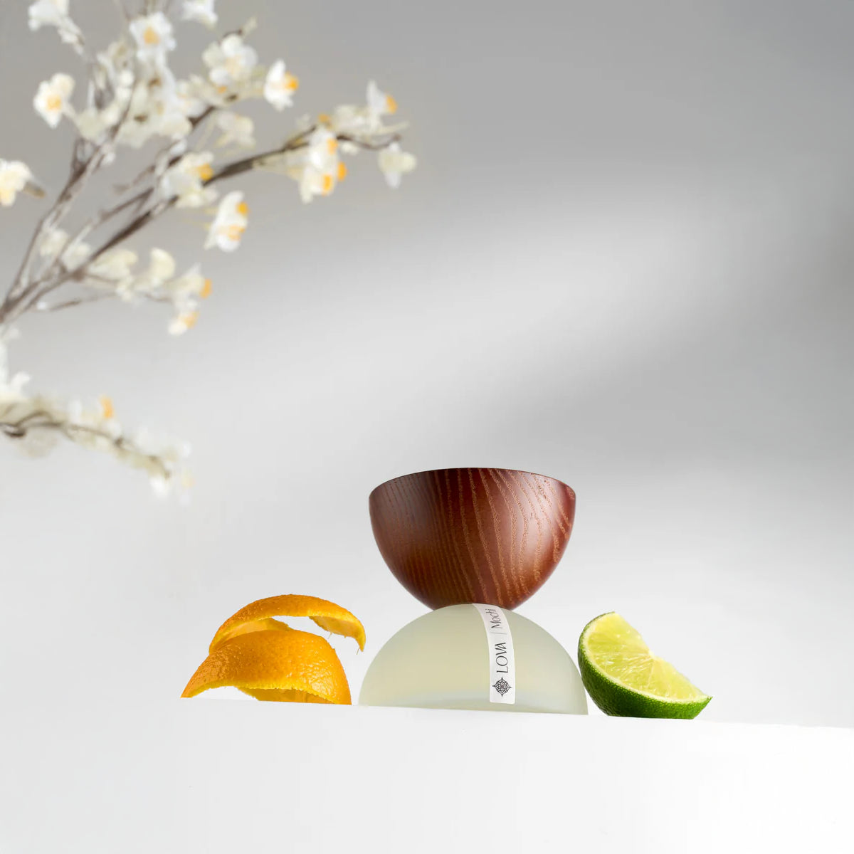 LOVA Mochi niche perfume with wooden cap and frosted white base styled with orange peel and lime slice in fresh citrus-inspired setting