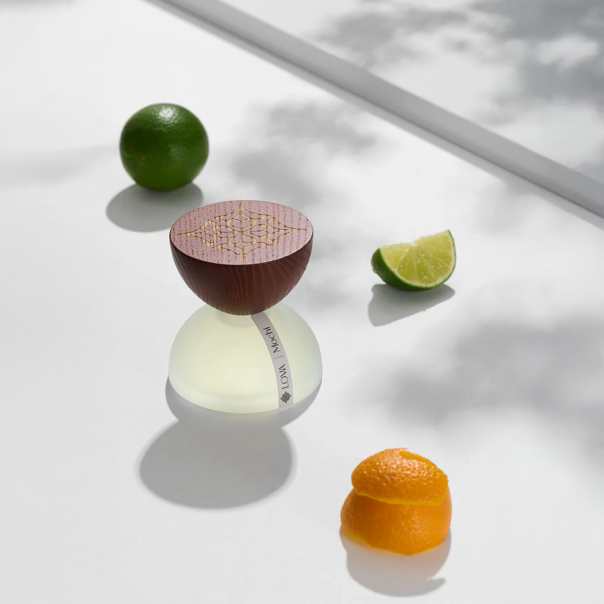 LOVA Mochi niche perfume bottle with engraved wooden cap and frosted base styled with fresh lime and orange peel in bright natural light