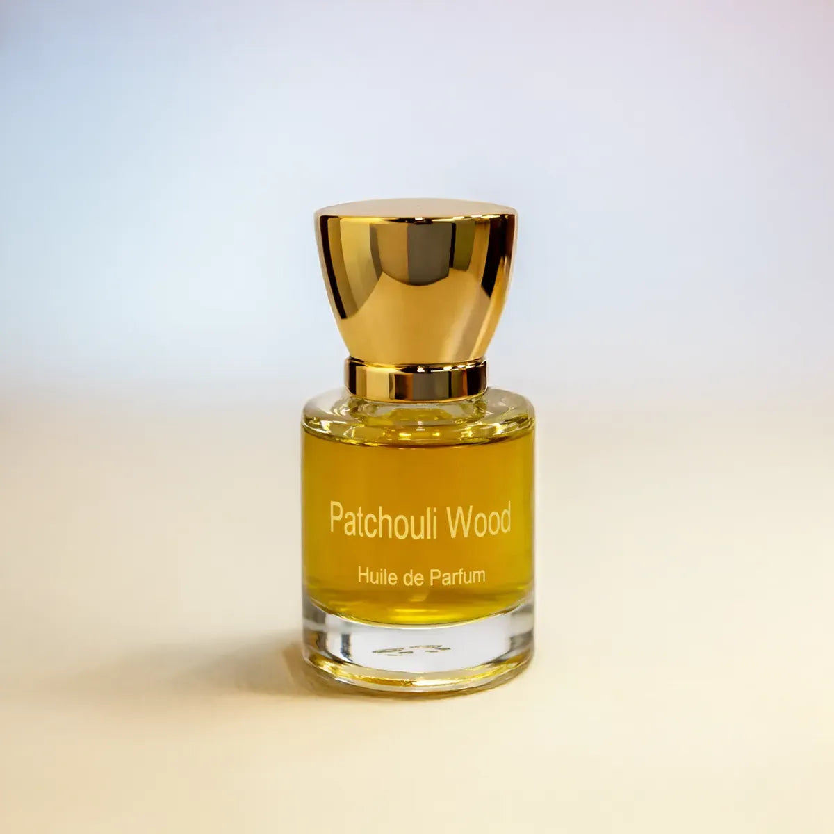 Patchouli Wood huile de parfum bottle with golden liquid and cap on soft gradient background