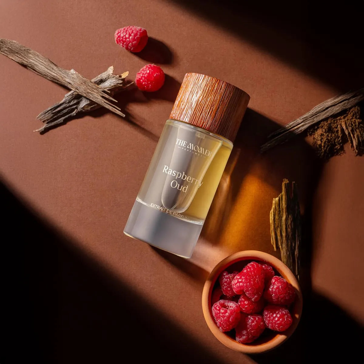 The Momer Raspberry Oud Extrait de Parfum with wooden cap styled with fresh raspberries and oud wood in warm luxury setting