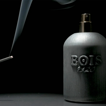 Bois 1920 Scuro perfume bottle with dark brushed metal finish and atomizer beside rising incense smoke on a black background.
