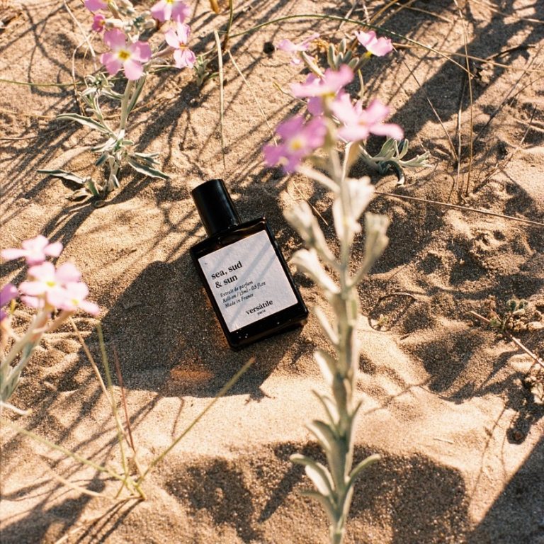 Versatile Paris Sea Sud & Sun perfume bottle placed on sandy ground surrounded by wildflowers