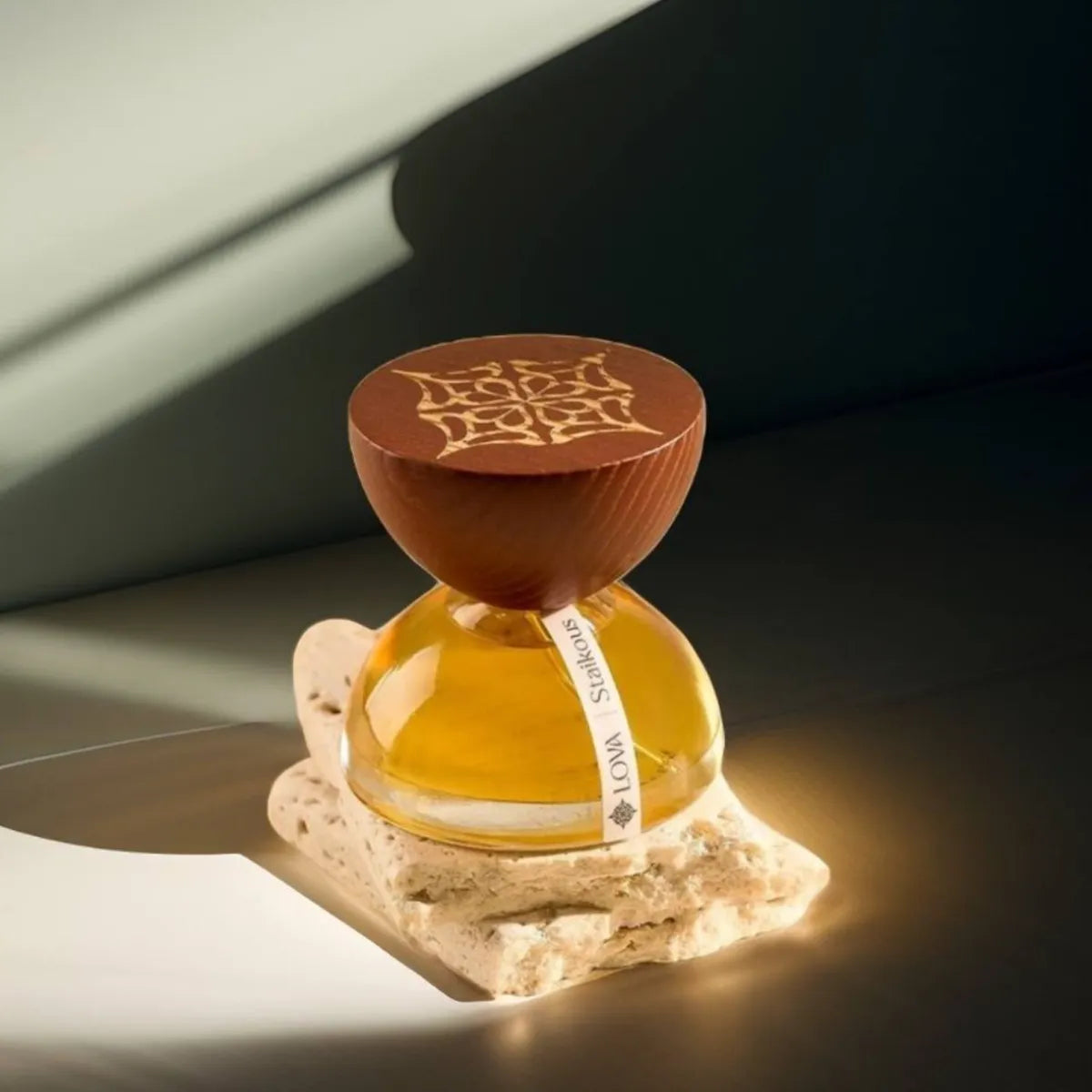 Staikous by LOVA luxury parfum bottle with golden glass base and engraved wooden cap displayed on stone surface in warm natural light
